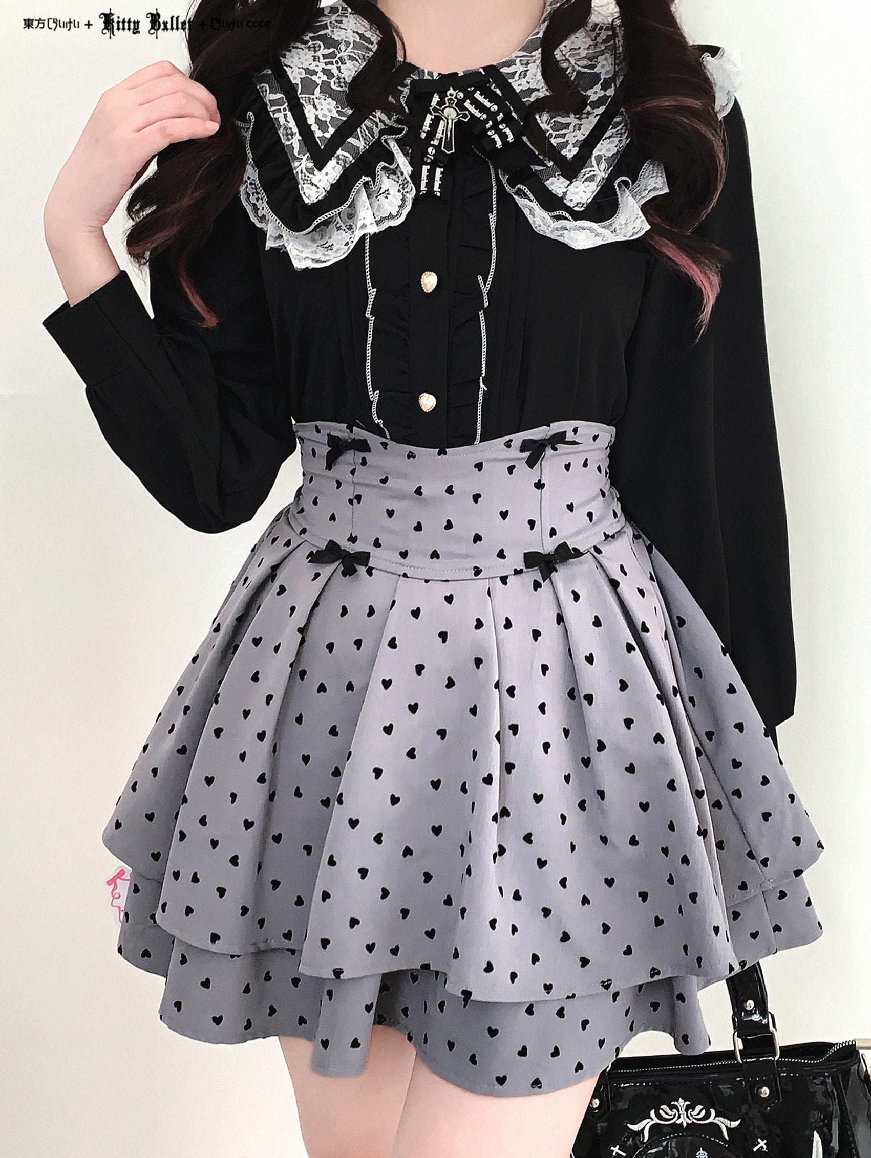 Person wearing a black blouse with lace details and a gray skirt with black heart patterns on a white background.