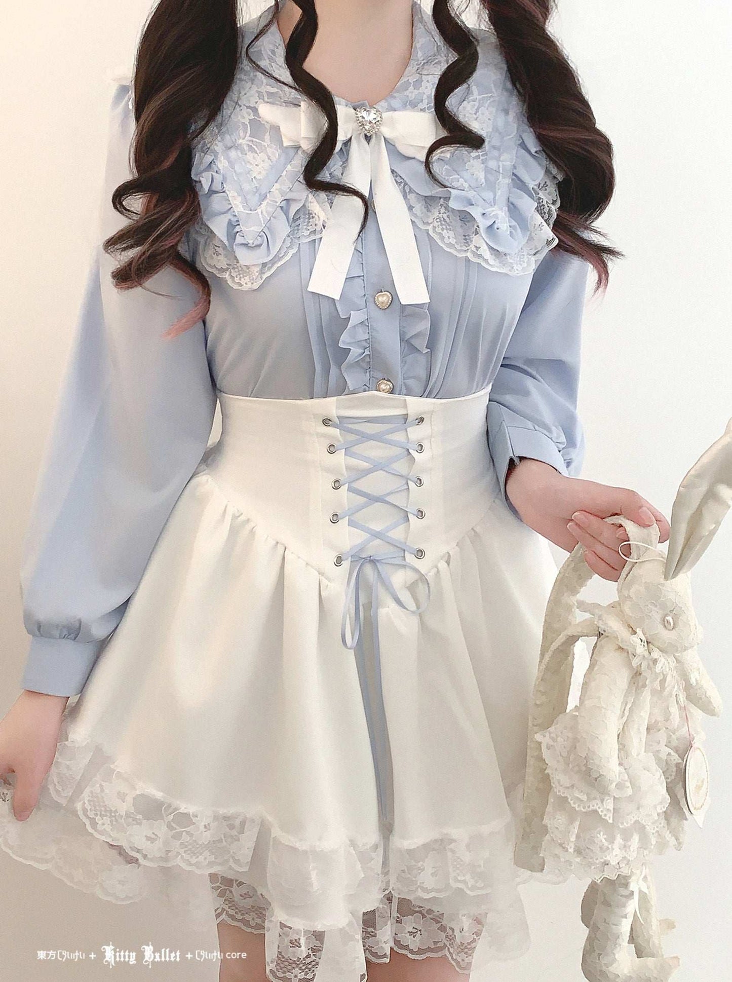 Person wearing a light blue blouse with lace details and a white skirt.