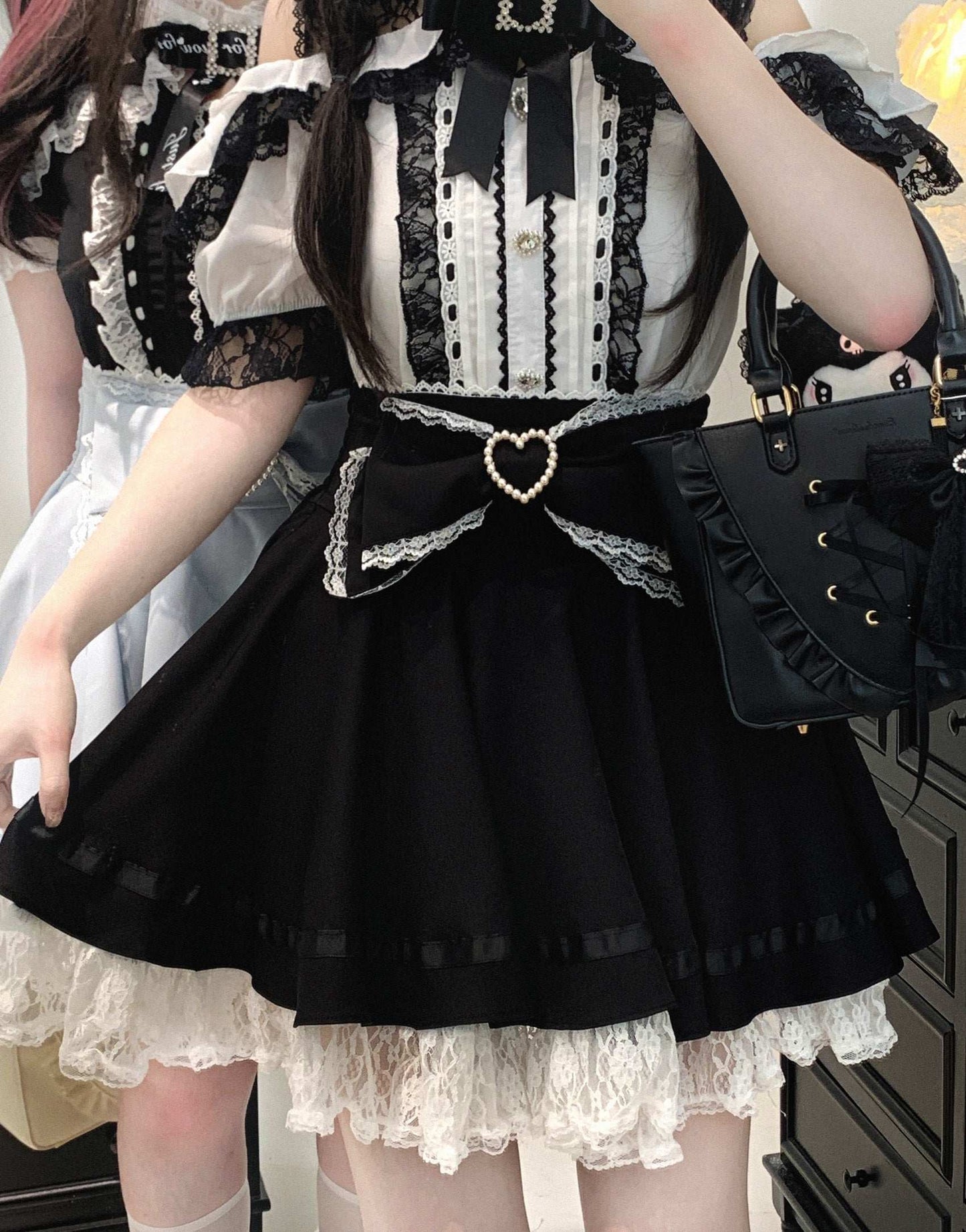 Person wearing a black and white outfit with a heart-shaped bow on the skirt, holding a black handbag.