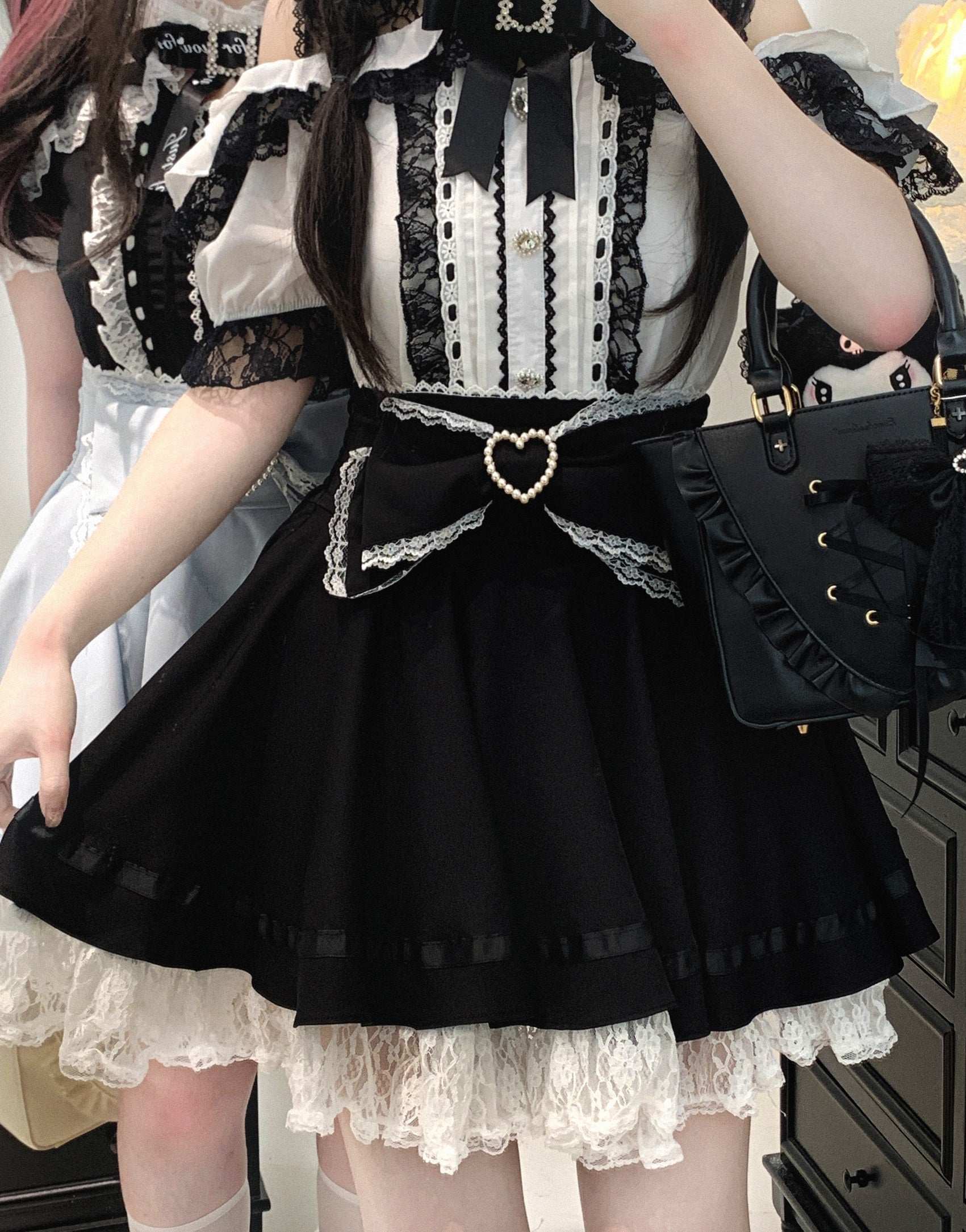 Person wearing a black and white outfit with a heart-shaped bow on the skirt, holding a black handbag.