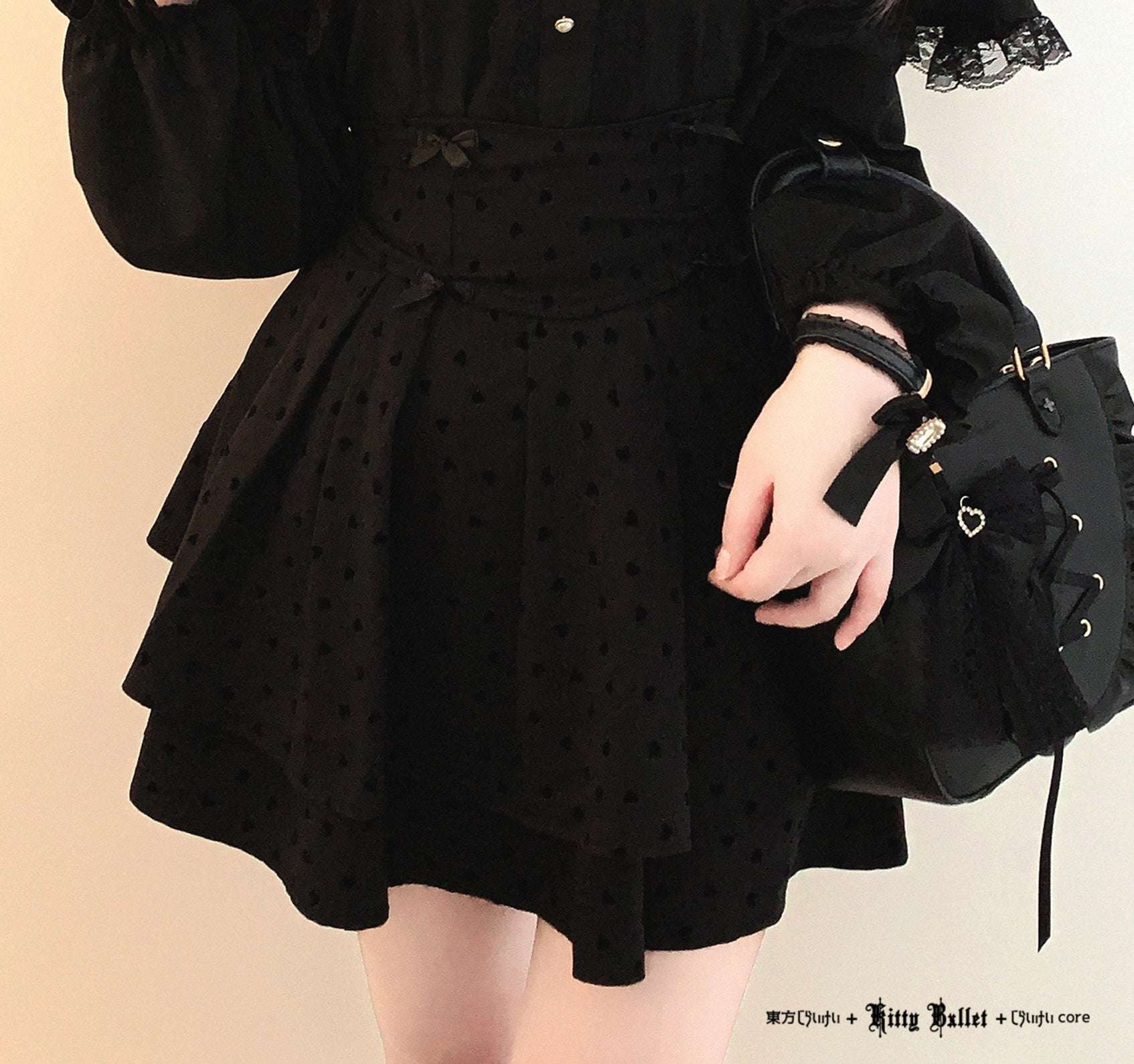 Person wearing a black polka dot dress holding a black bag with a bow on a beige background