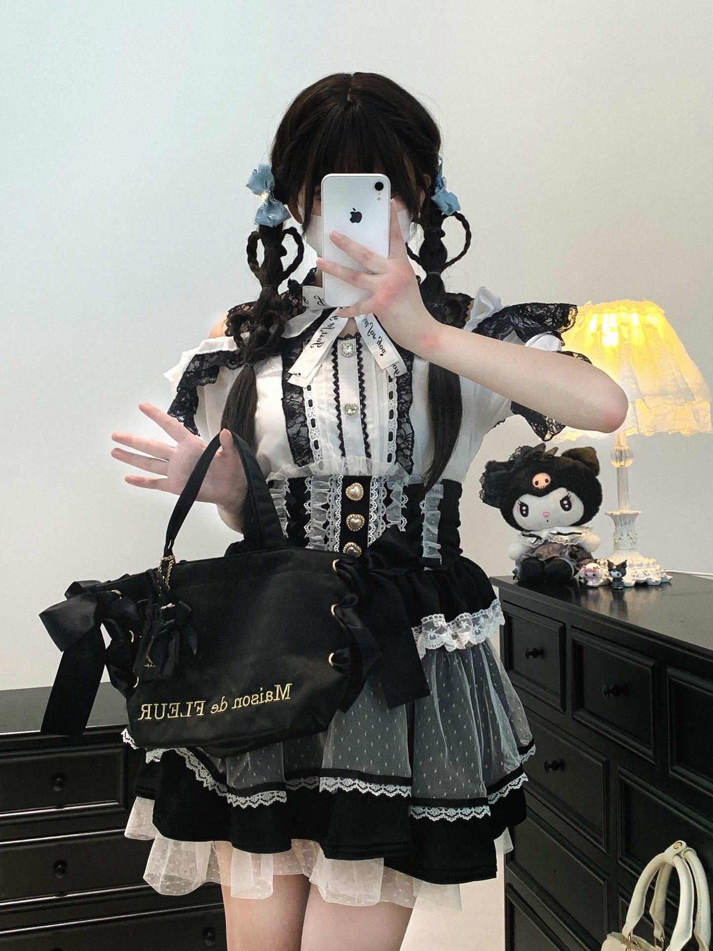 Person wearing a black and white outfit with a black bag, standing in front of a mirror.