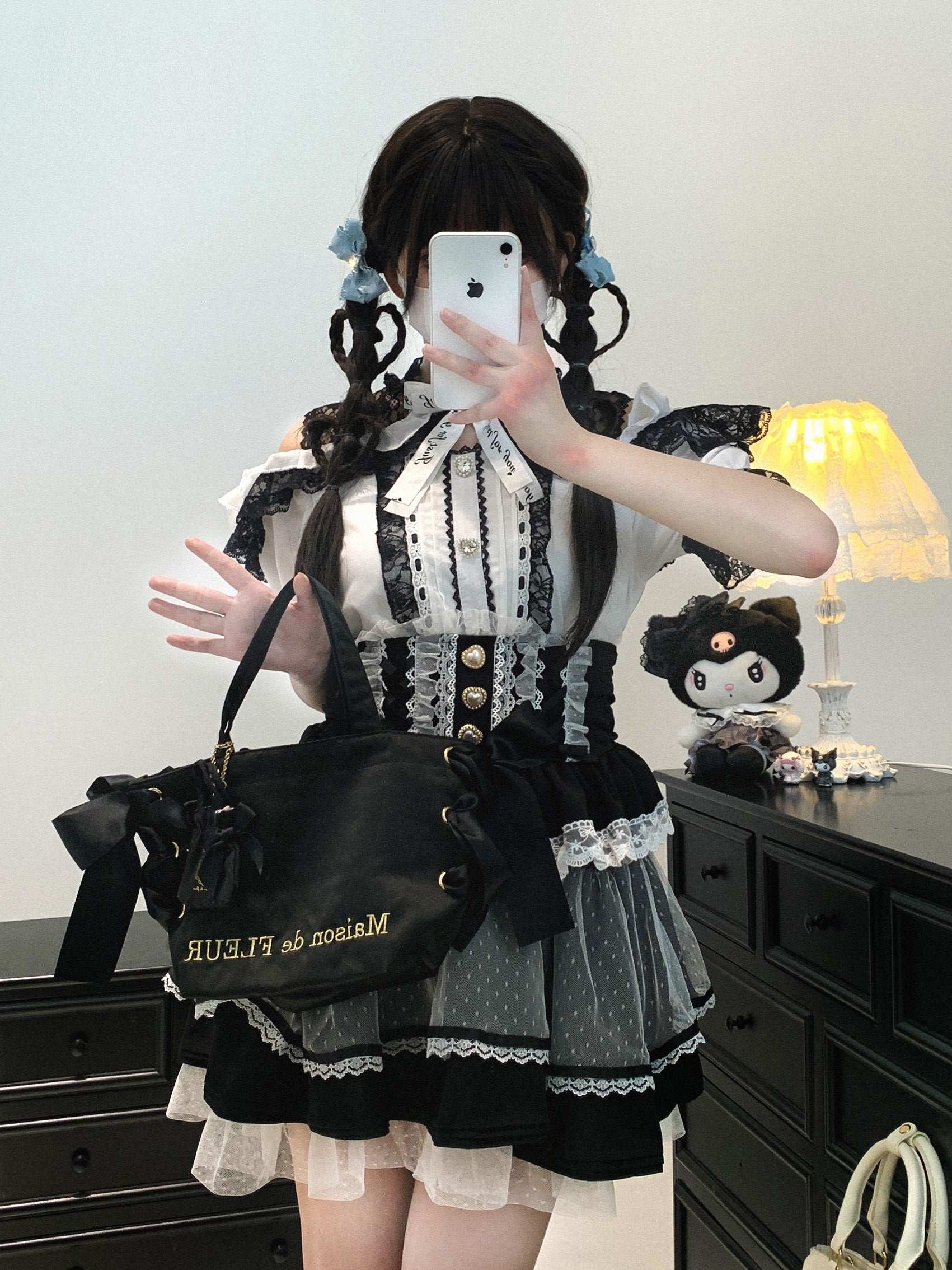 Person wearing a black and white outfit with a black bag, standing in front of a mirror.