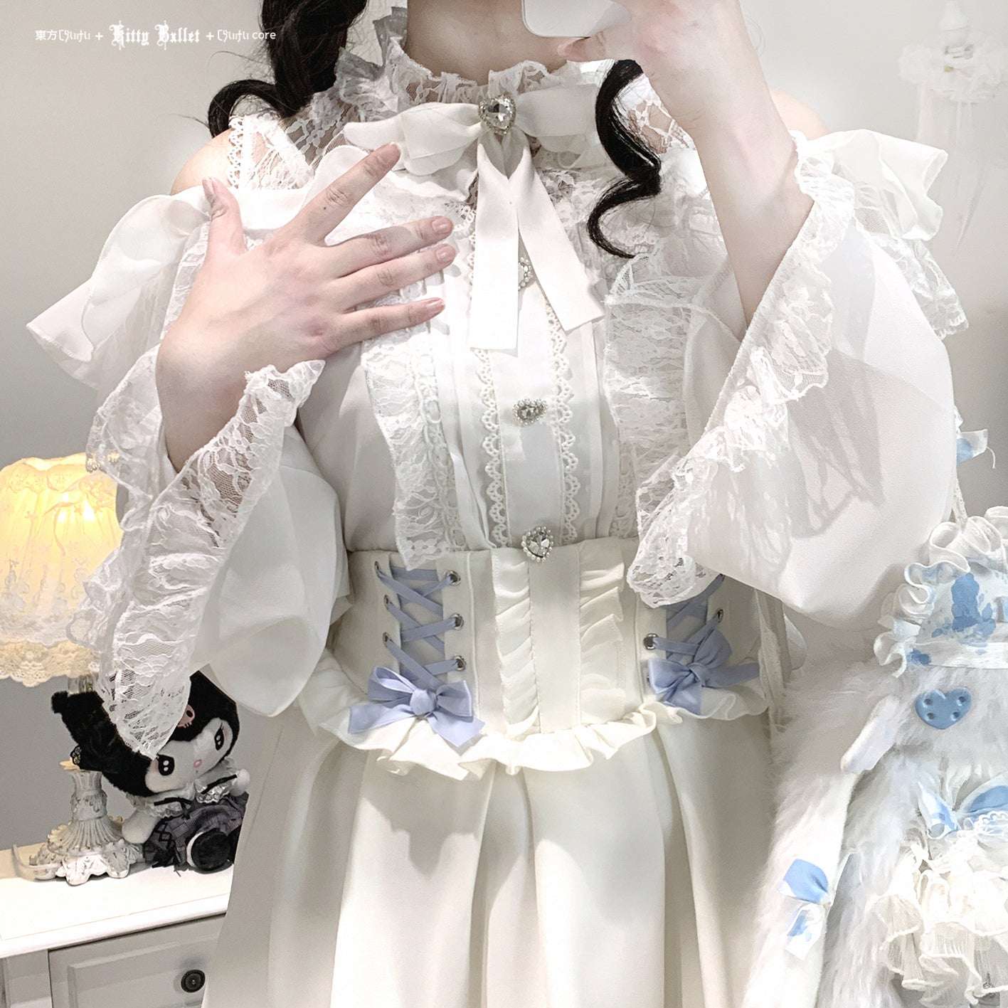 Person wearing a white ruffled outfit with decorative elements in jirai kei style, holding a plush toy.