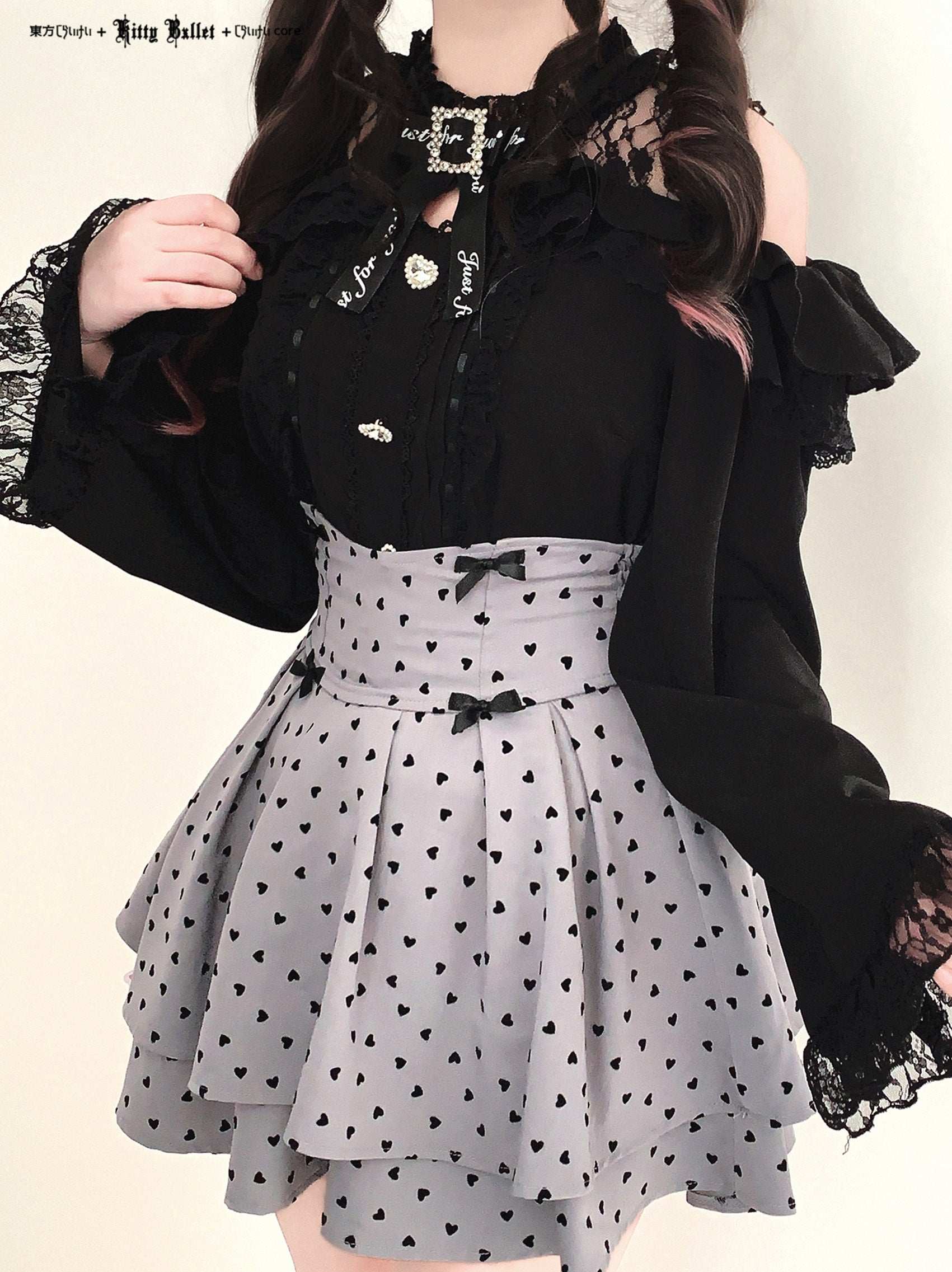 Person wearing a black top with lace details and a gray skirt in jirai kei style with black heart patterns.