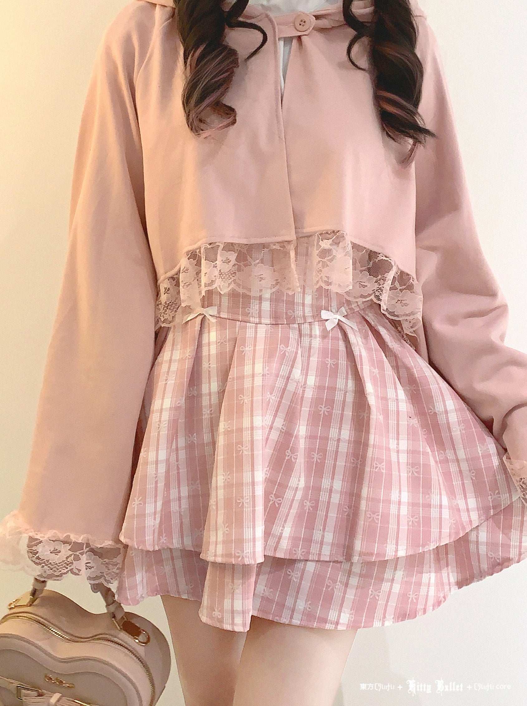 Person wearing a pink outfit with a plaid skirt and lace details on a plain background