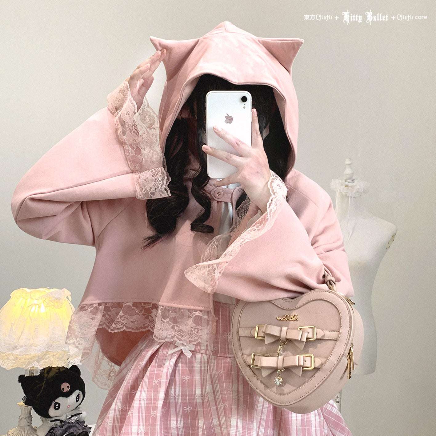 Person wearing a pink hoodie with cat ears, holding a phone, and carrying a heart-shaped bag.