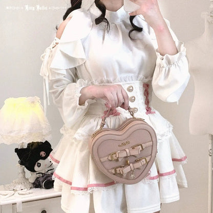 Person wearing a white dress with ruffles holding a pink heart-shaped bag.
