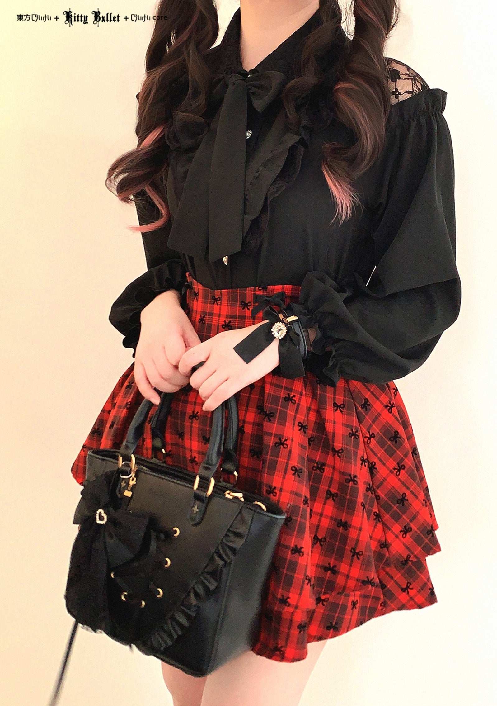 Person wearing a black blouse jirai kei style with ruffled sleeves and a red plaid skirt, holding a black handbag.
