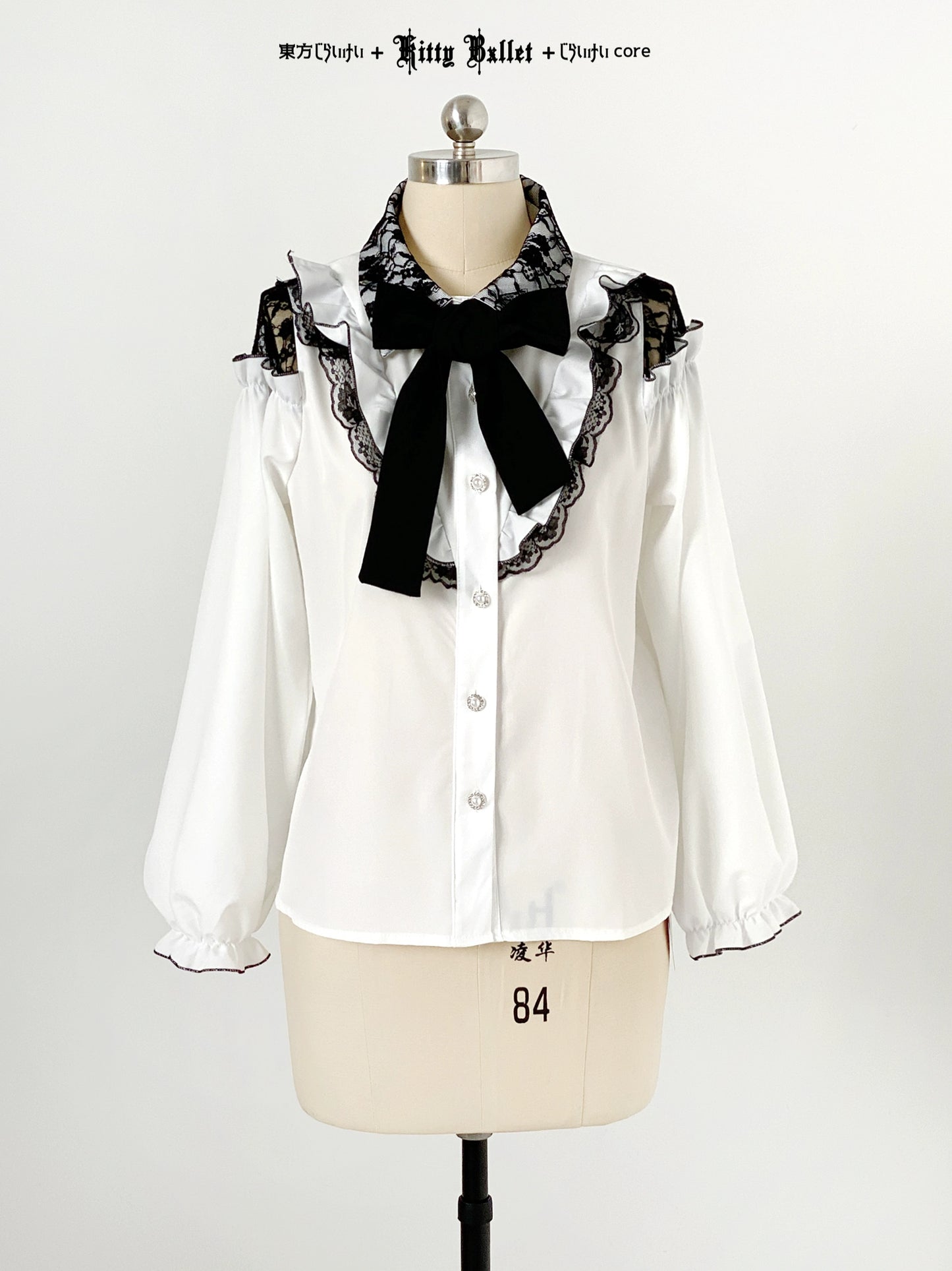White blouse jirai kei style with black lace and bow on a mannequin against a white background