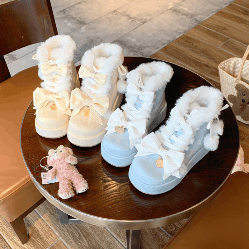 Pair of white and blue fluffy shoes on a round wooden table with a small pink teddy bear beside them.