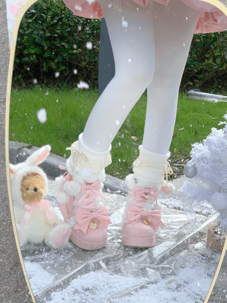Pink boots with bows worn by a person, standing on a stone surface with a blurred outdoor background.