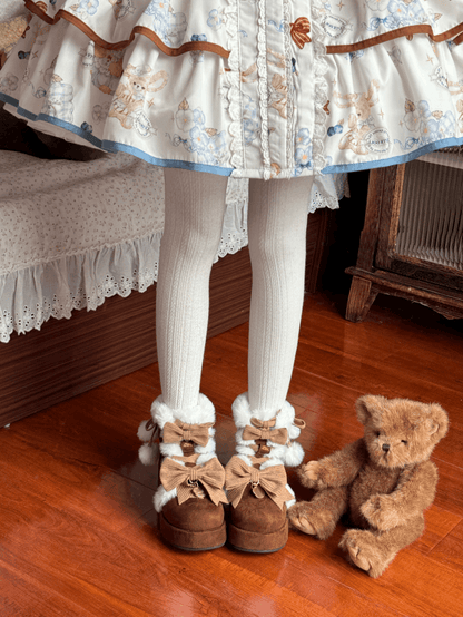 Person wearing a floral dress, white tights, and brown boots with bows, standing next to a teddy bear on a wooden floor.