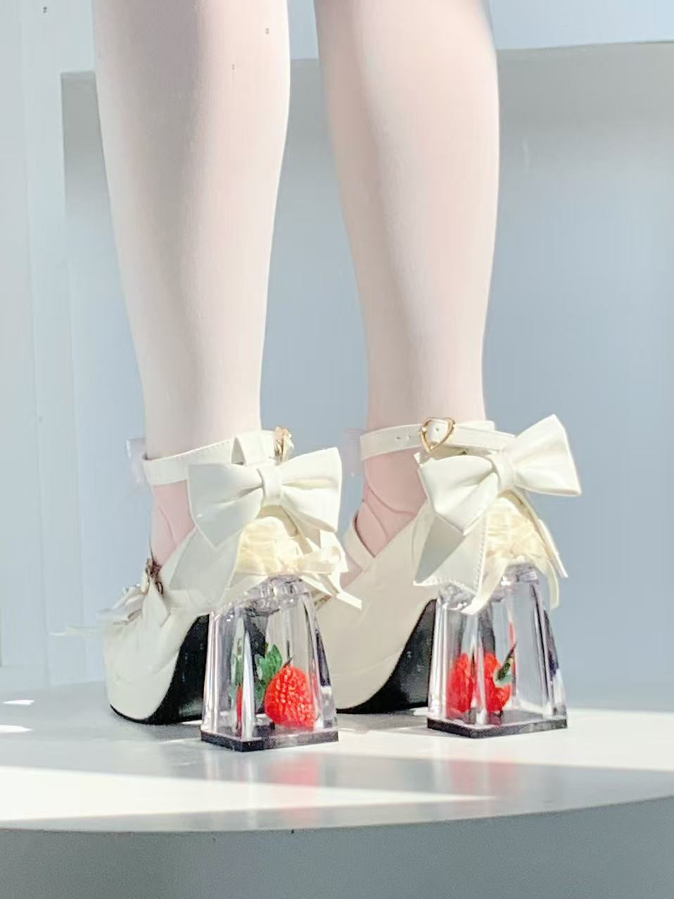 White high-heeled shoes with large bows and clear platforms on a light background