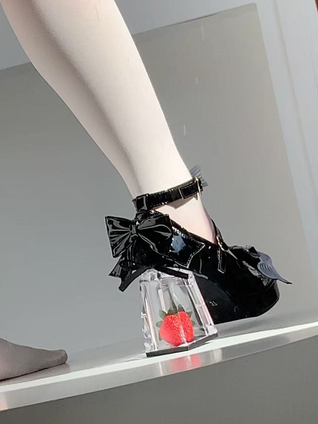 Black patent leather shoes with large bows and clear heels on a gray background