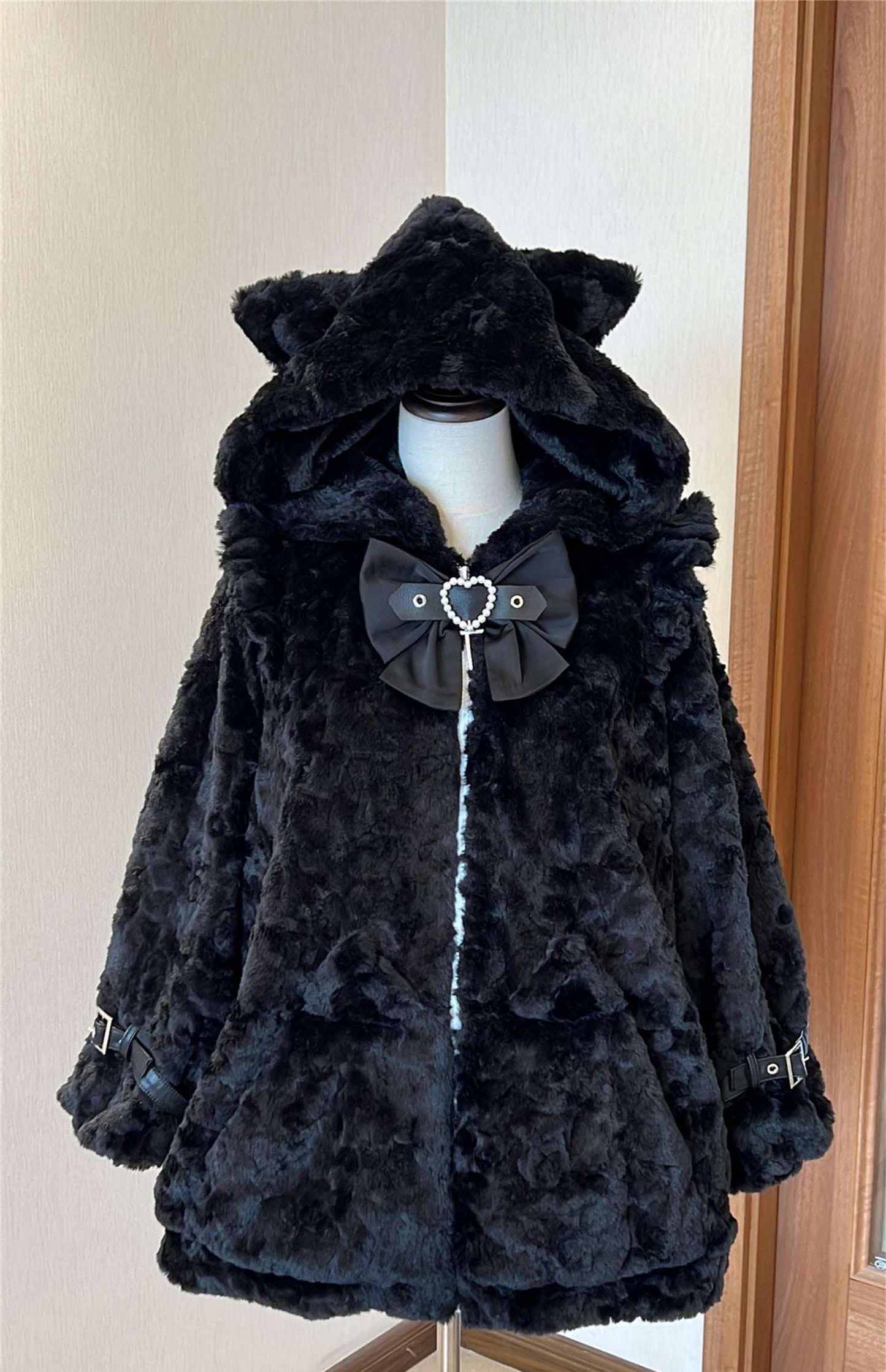 Black faux fur coat with a large bow on a mannequin against a neutral wall.