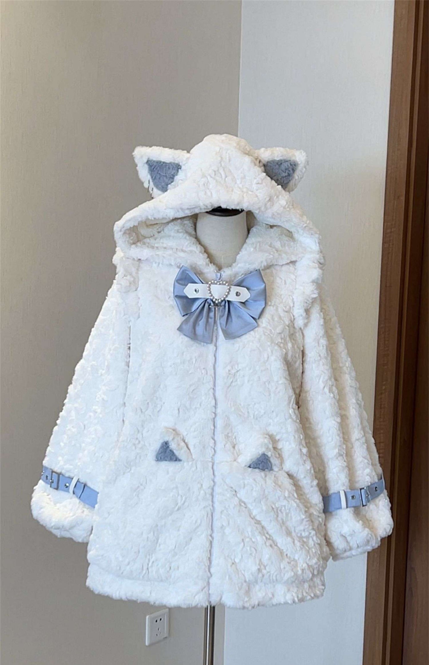 White plush jacket with cat ears and a bow on a mannequin against a neutral wall.