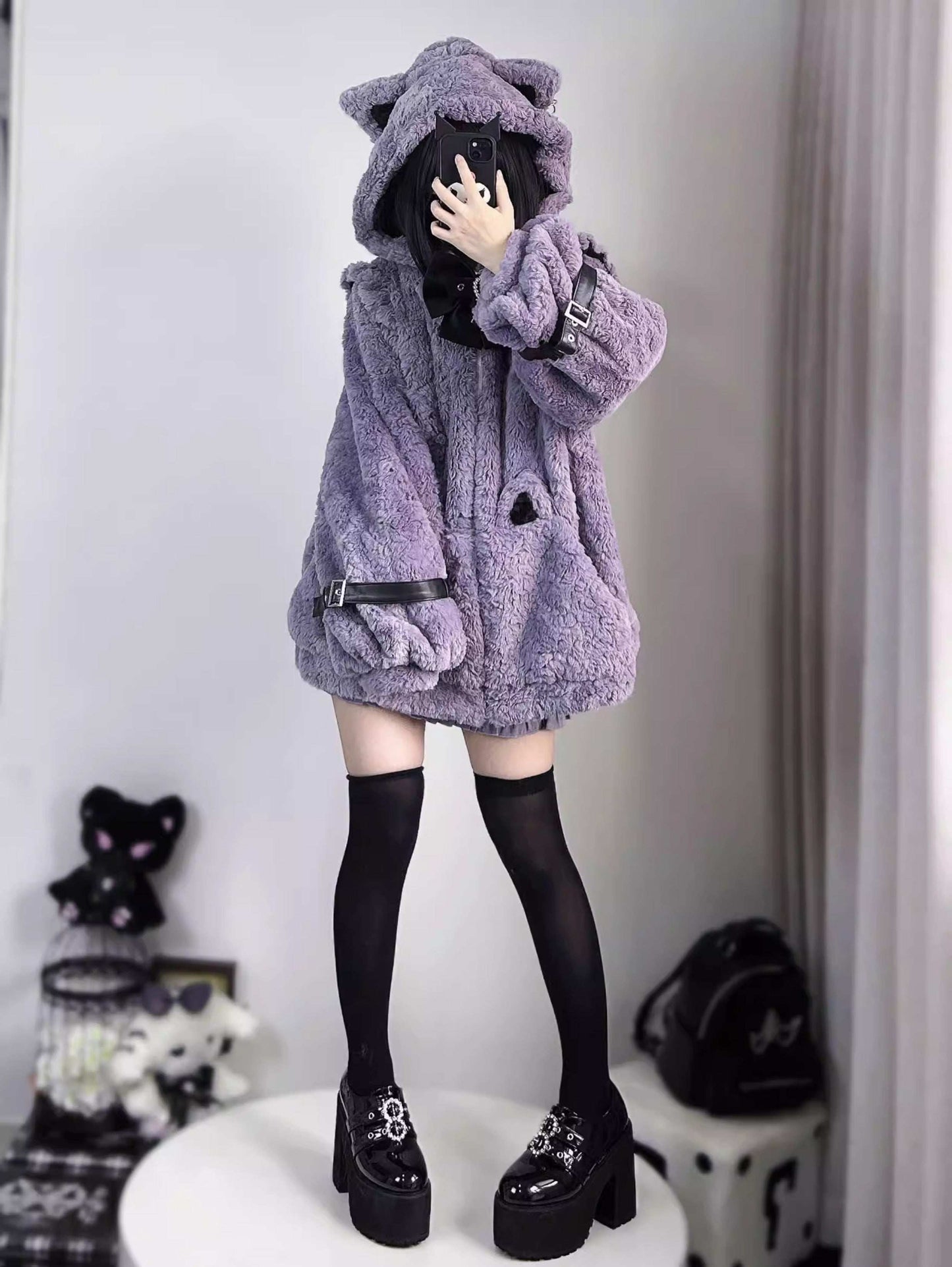 Person wearing a fluffy purple coat with a hood in a room setting.