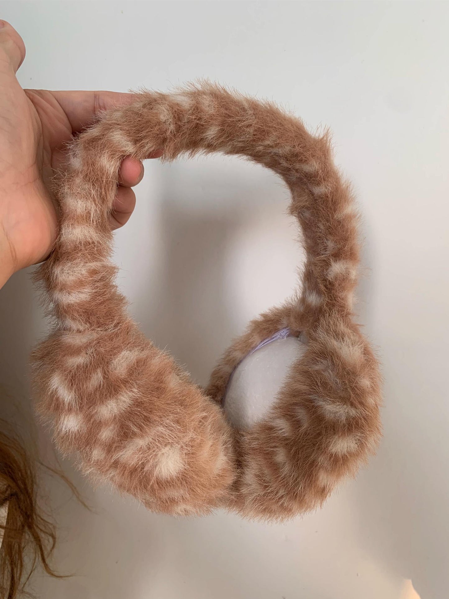 Brown fur-like headband held by a hand on a white background