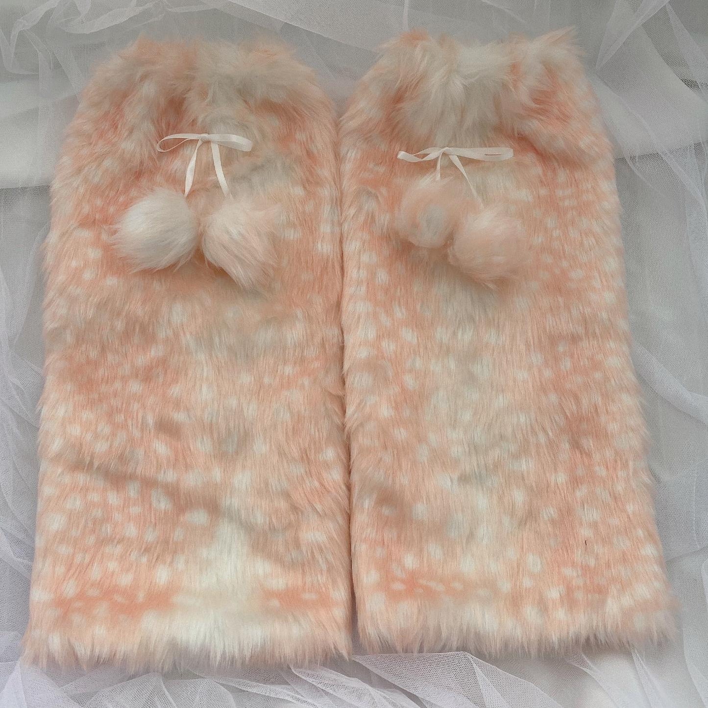 Two pink fluffy deer pattern leg warmers with white pom-poms on a light gray background