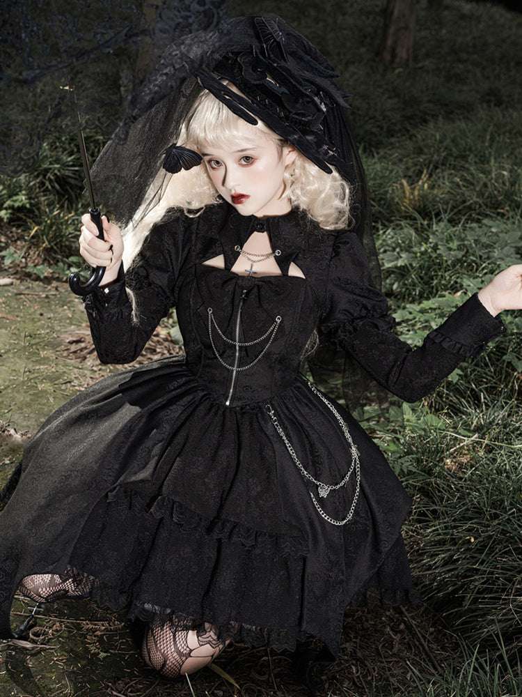 Person in a black gothic dress with a hood sitting on grass.