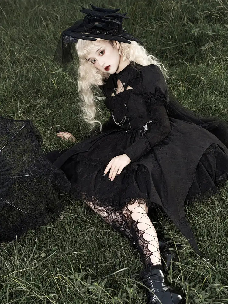 Person in a black gothic outfit sitting on grass