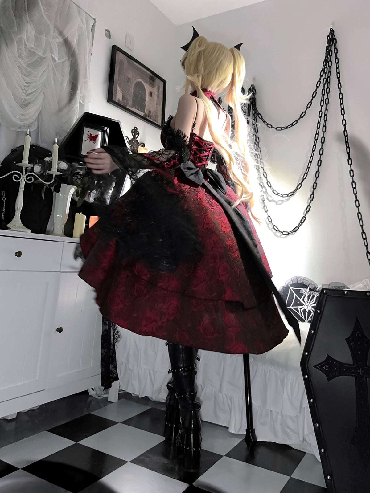 Person in a red and black outfit with long blonde hair in a room with decorative chains and furniture.