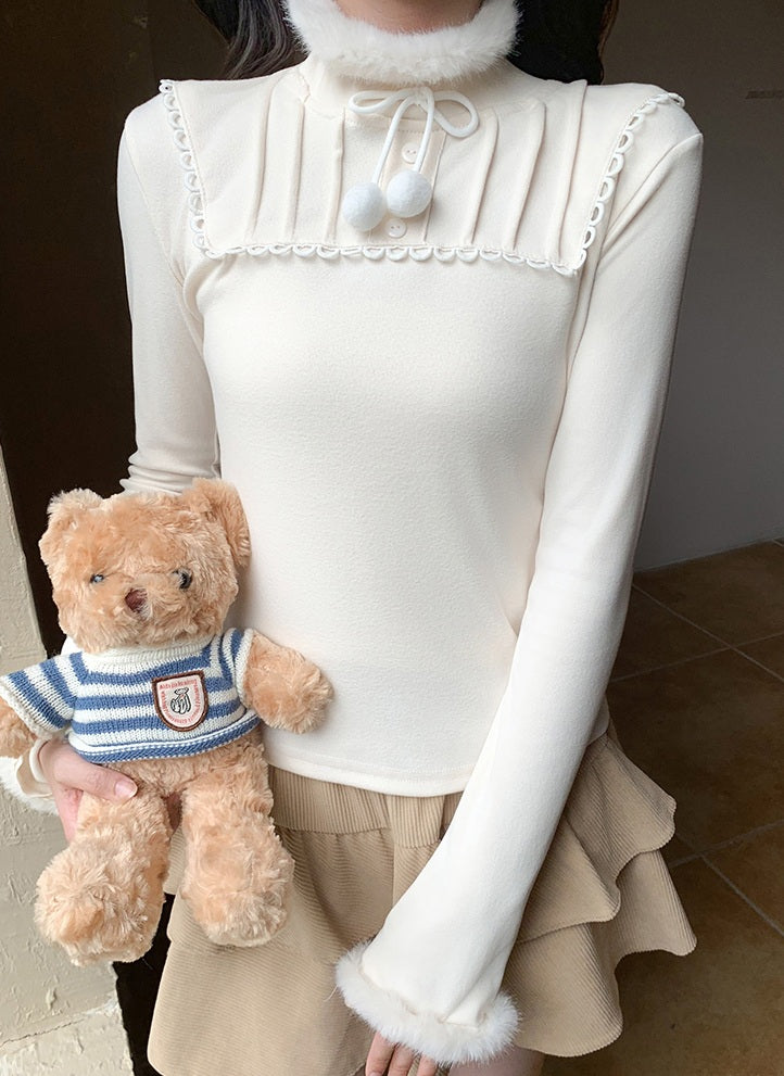 Person wearing a white long-sleeve top with pearl details holding a teddy bear.