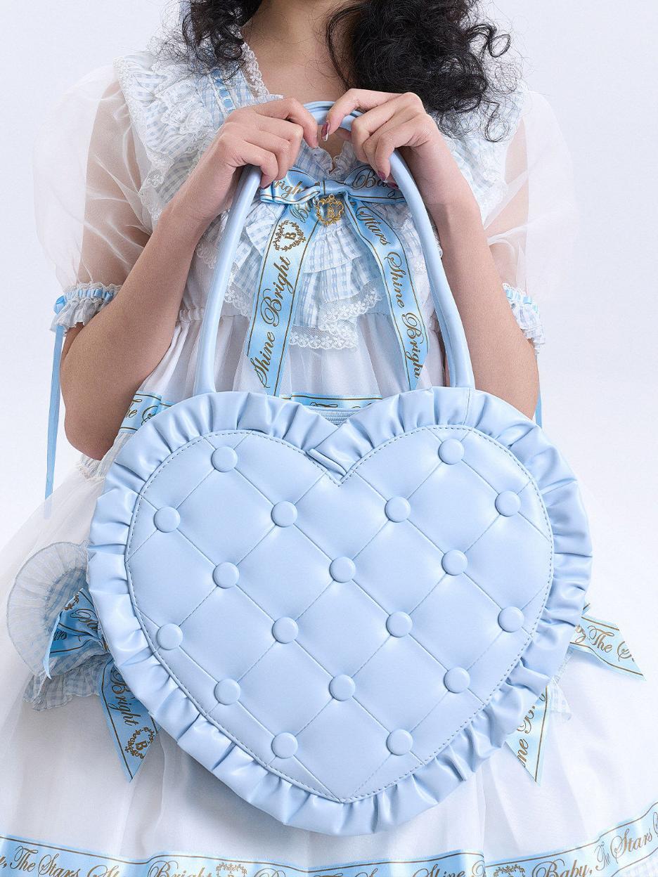 Light blue heart-shaped bag with ruffles held by a person against a white background