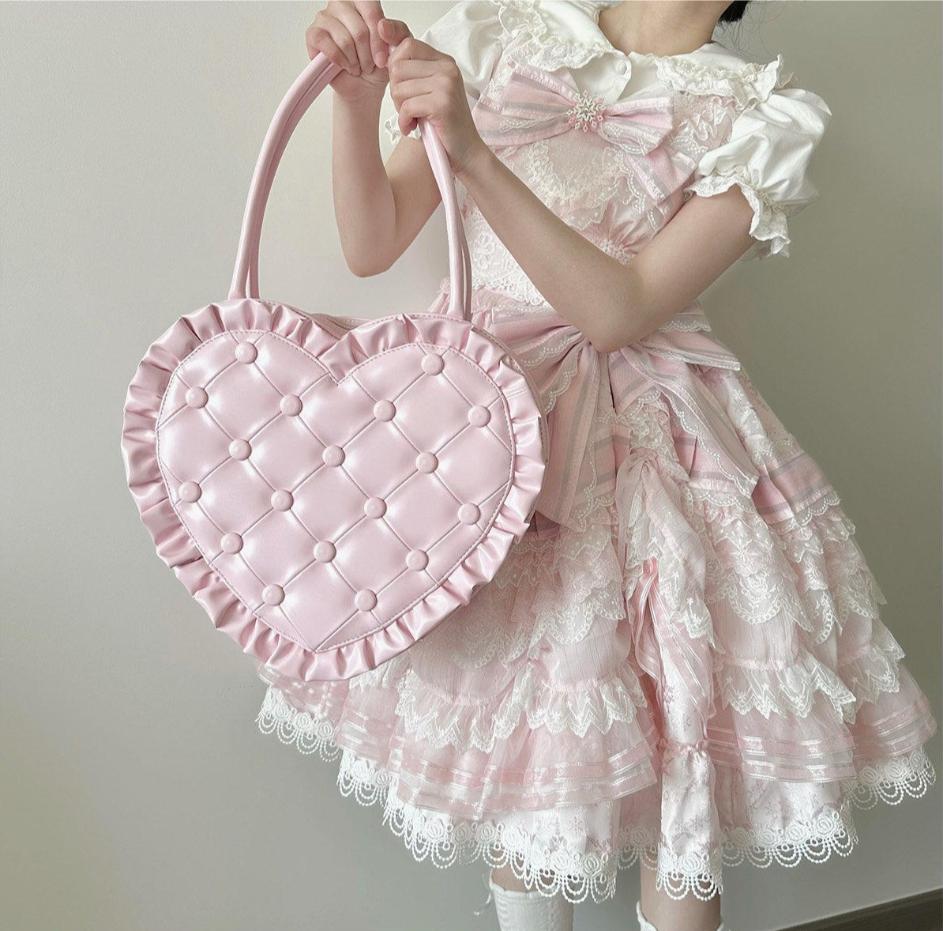 Person wearing a pink and white dress holding a pink heart-shaped bag.
