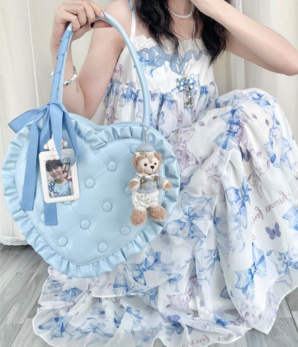 Person holding a light blue heart-shaped bag with a teddy bear charm, wearing a floral dress.