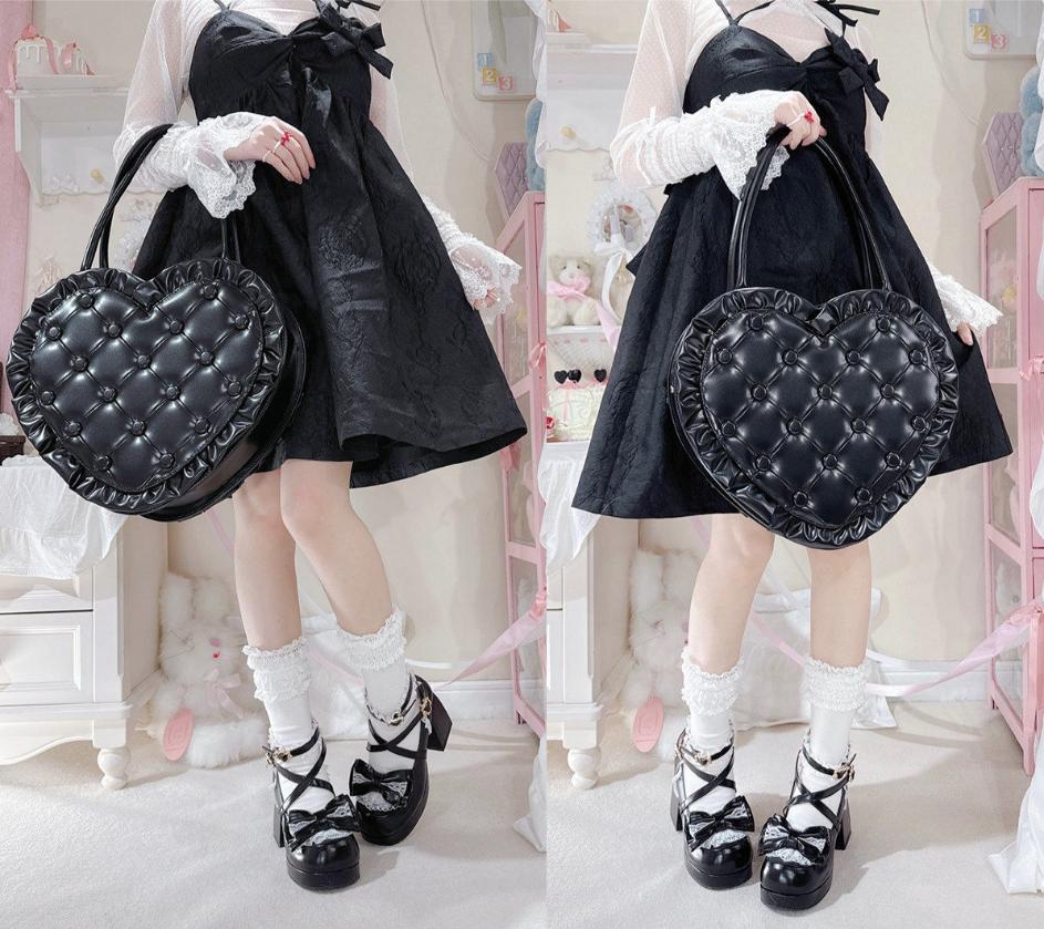 Person wearing a black dress with white lace details, holding a black heart-shaped bag in a pastel room.