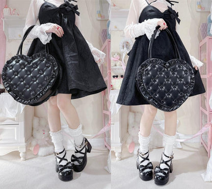 Person wearing a black dress with white lace details, holding a black heart-shaped bag in a pastel room.