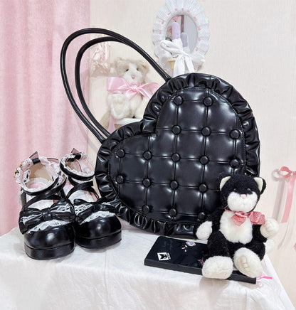 Black quilted handbag, black shoes with white bows, and a small black and white teddy bear on a light pink background.
