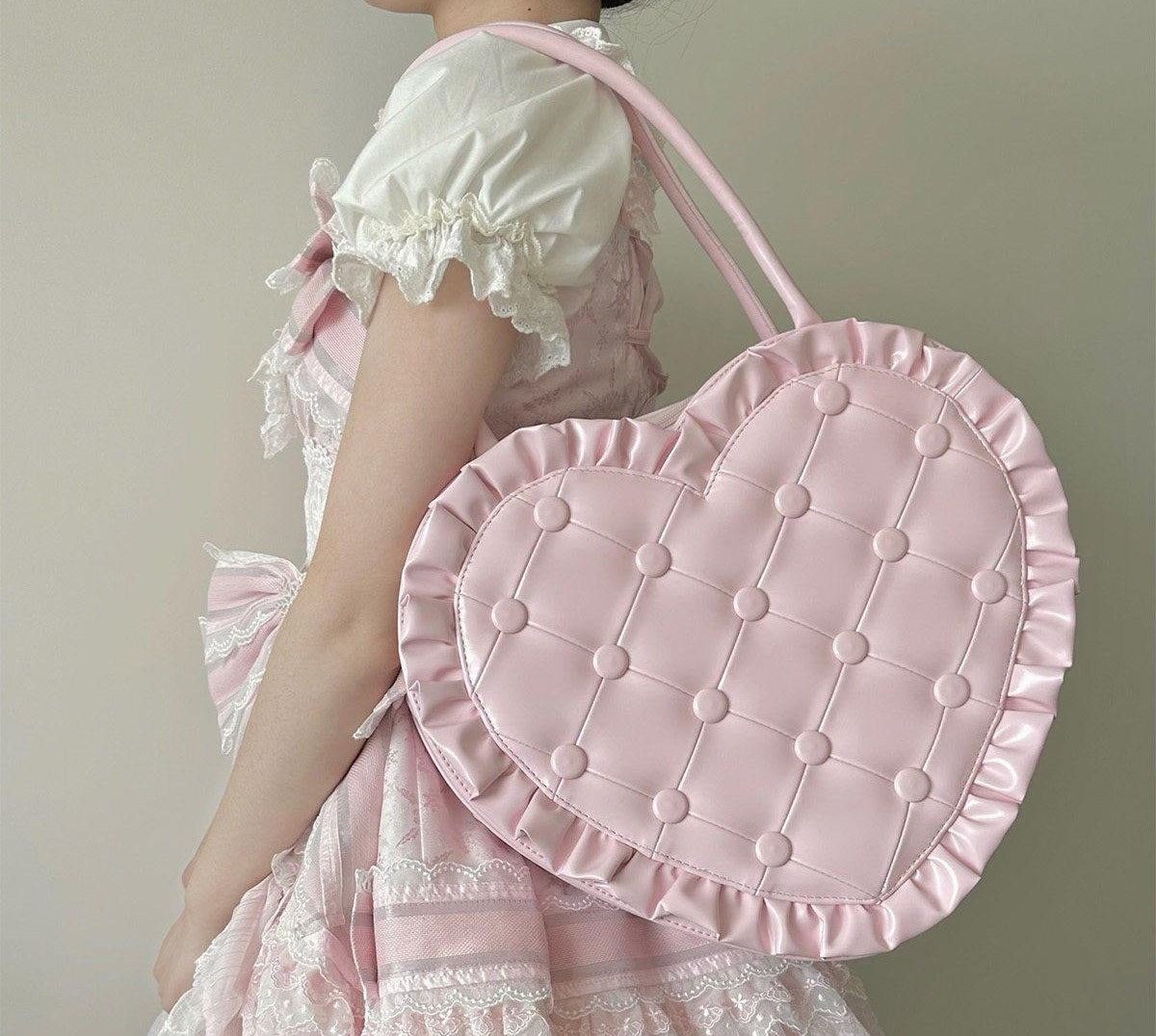 Person wearing a pink dress holding a matching pink heart-shaped bag against a neutral background