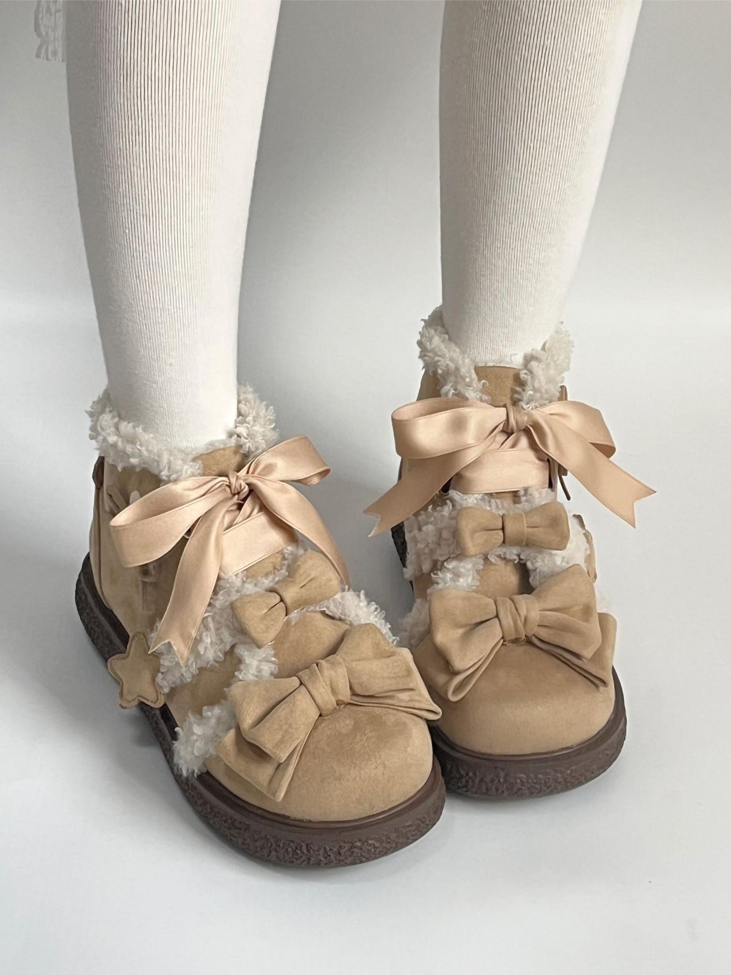 Tan suede lolita style shoes with large bows worn with white tights on a light gray background