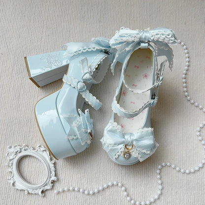 Pair of light blue high-heeled shoes with decorative bows and lace on a beige surface.