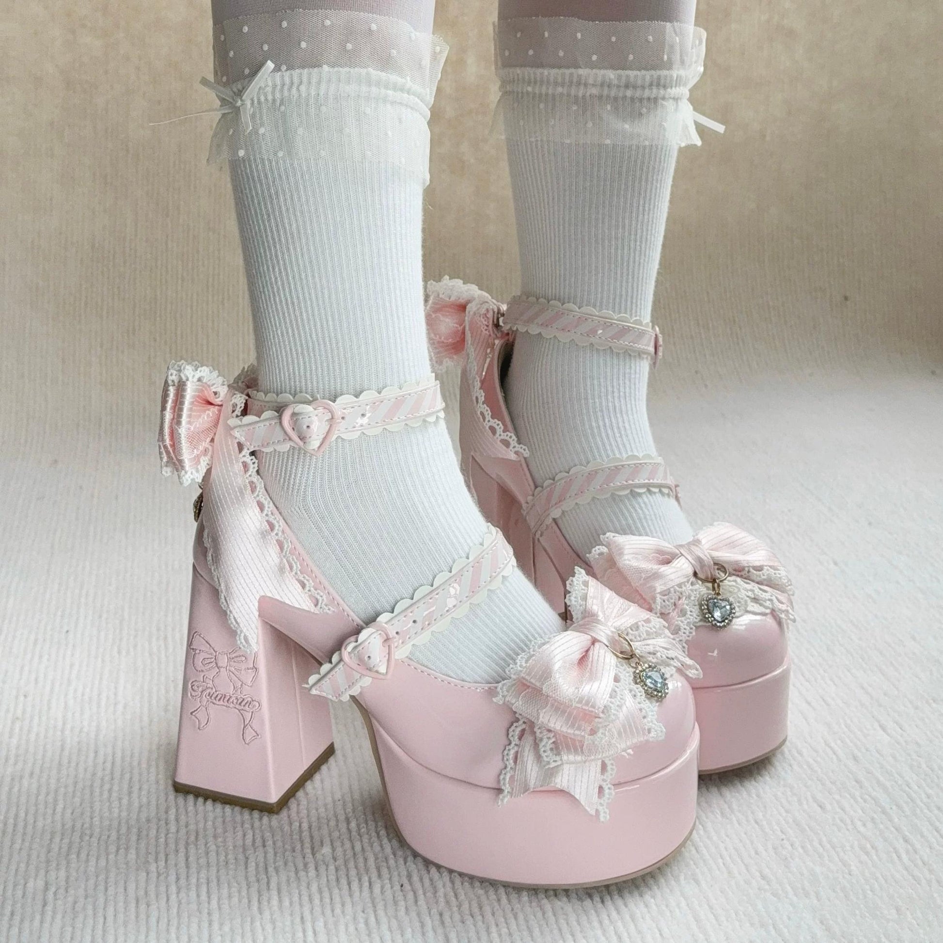 Pink platform shoes with decorative bows worn with white socks on a neutral background
