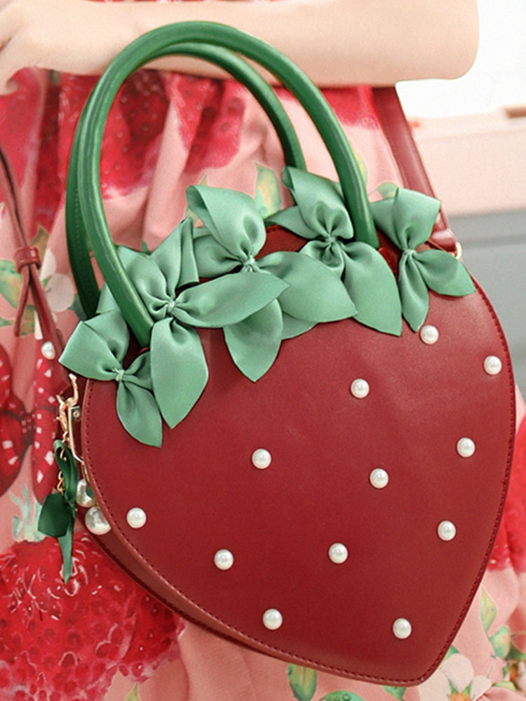Strawberry-shaped handbag with green bows and white dots held by a person.