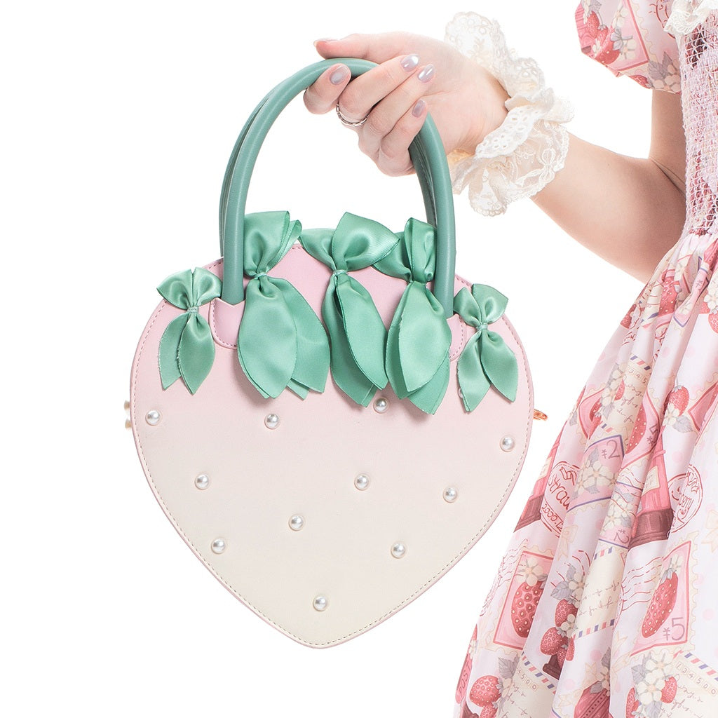 Heart-shaped handbag with green ribbons held by a person wearing a floral dress.
