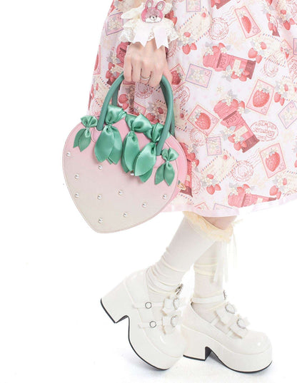 Person holding a pink heart-shaped handbag with green handles, wearing a patterned dress and white boots.