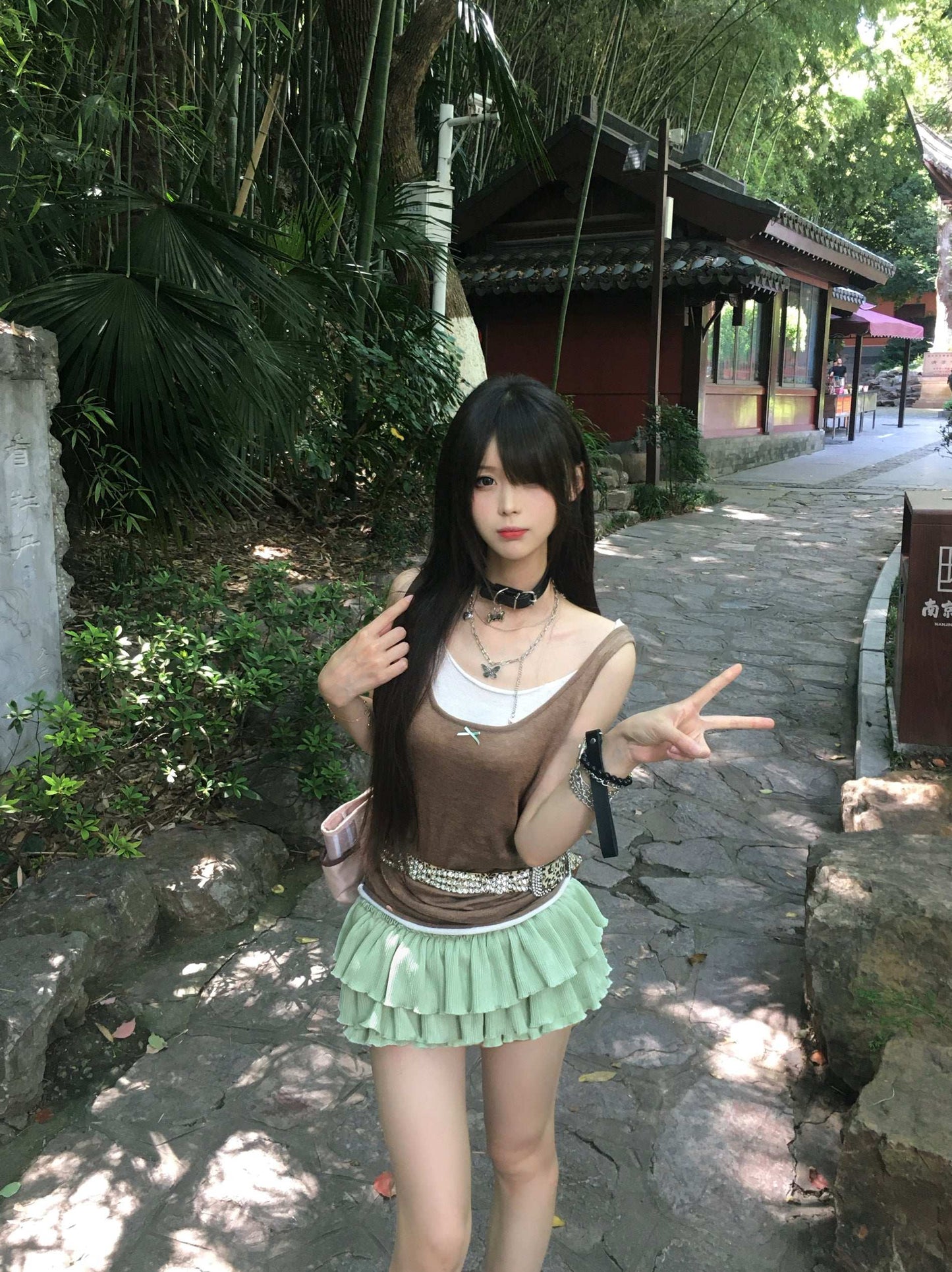Woman posing outdoors in a scenic area with greenery and traditional architecture.