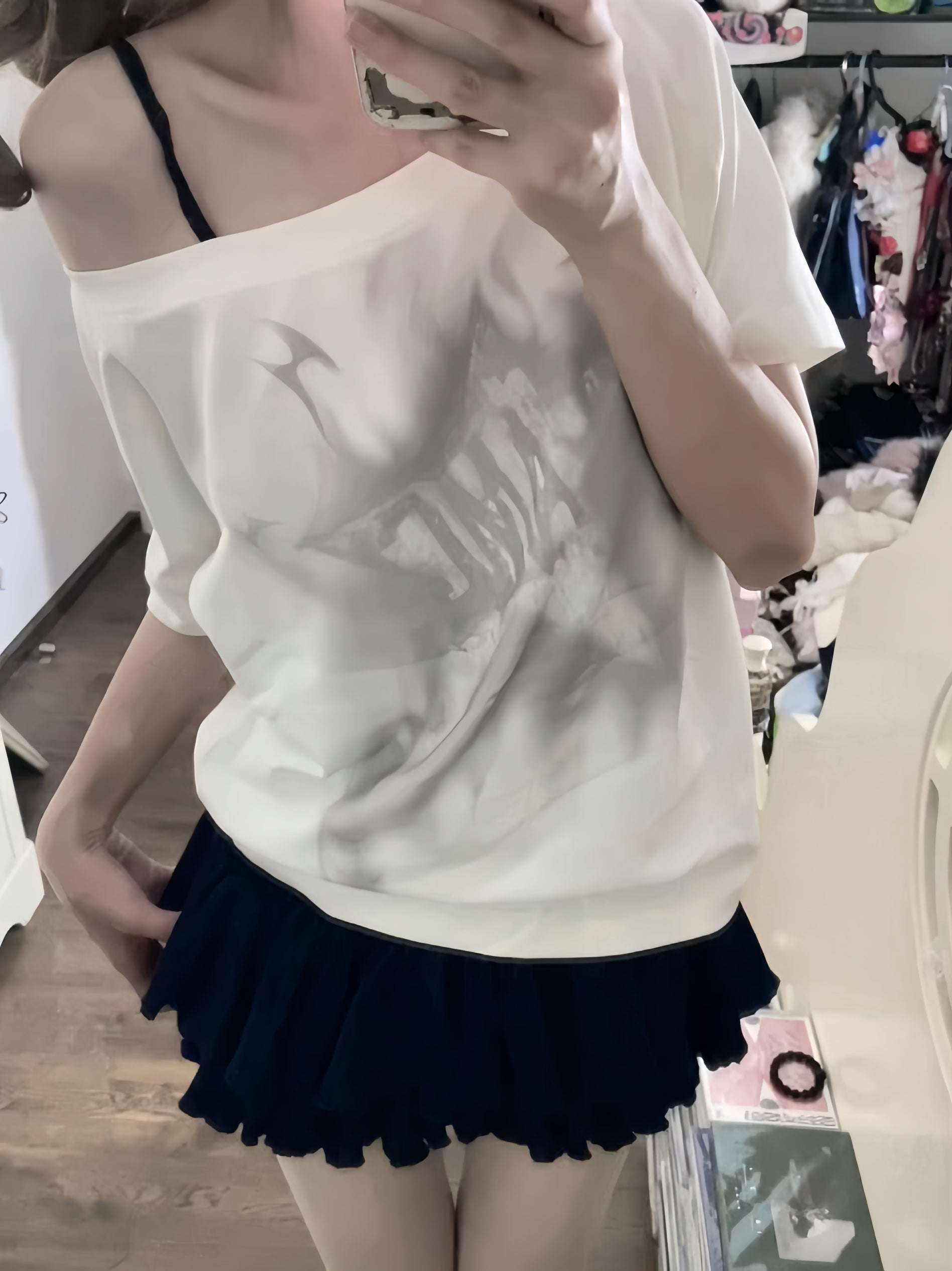 Person wearing a white off-shoulder top and navy skirt in an indoor setting.