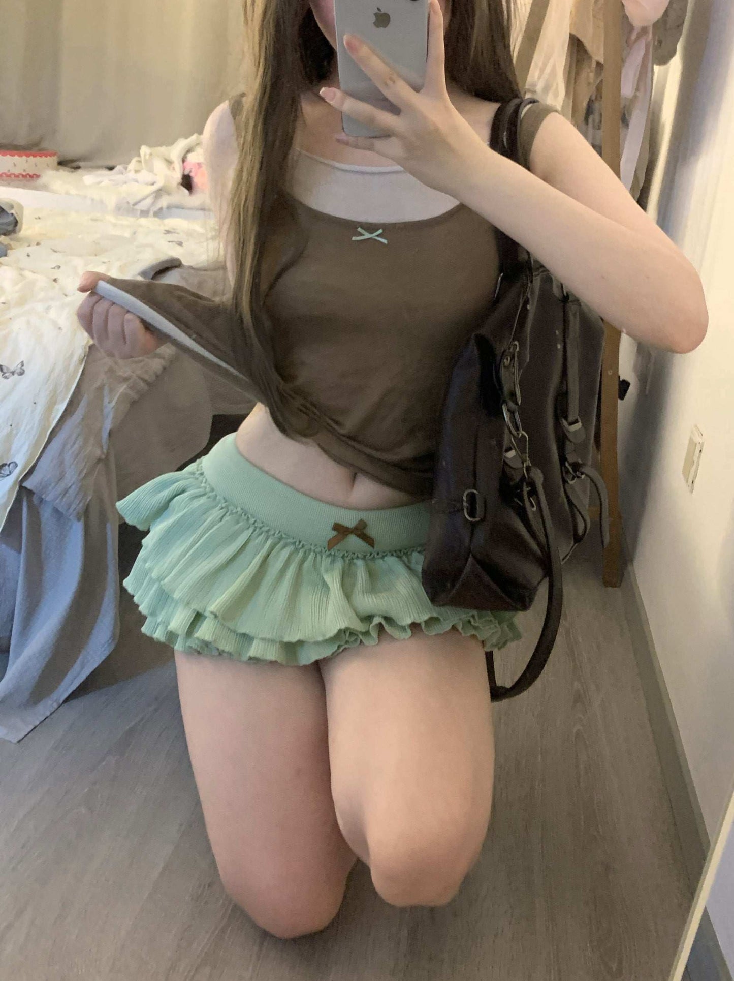 Person wearing a brown top and green skirt with a backpack, taking a mirror selfie.