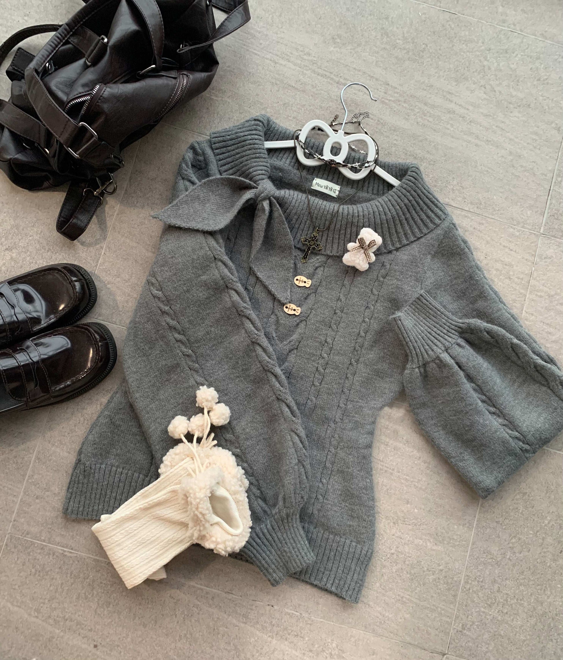 Gray cable knit sweater with decorative elements on a textured surface