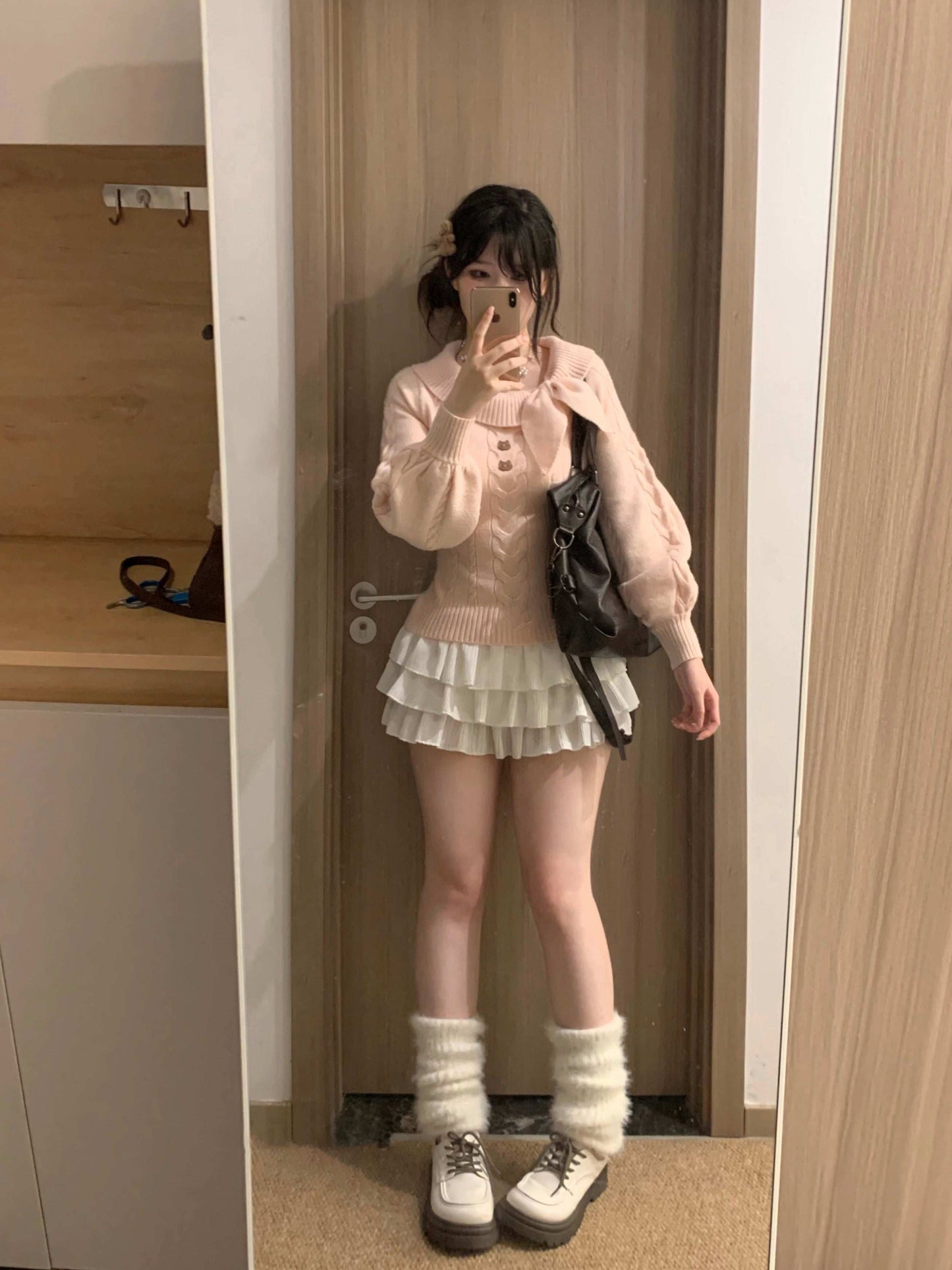Person taking a mirror selfie wearing a white sweater, skirt, and shoes in a room.