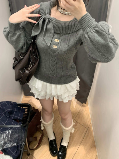 Person wearing a gray sweater with a bow and white skirt in a room.