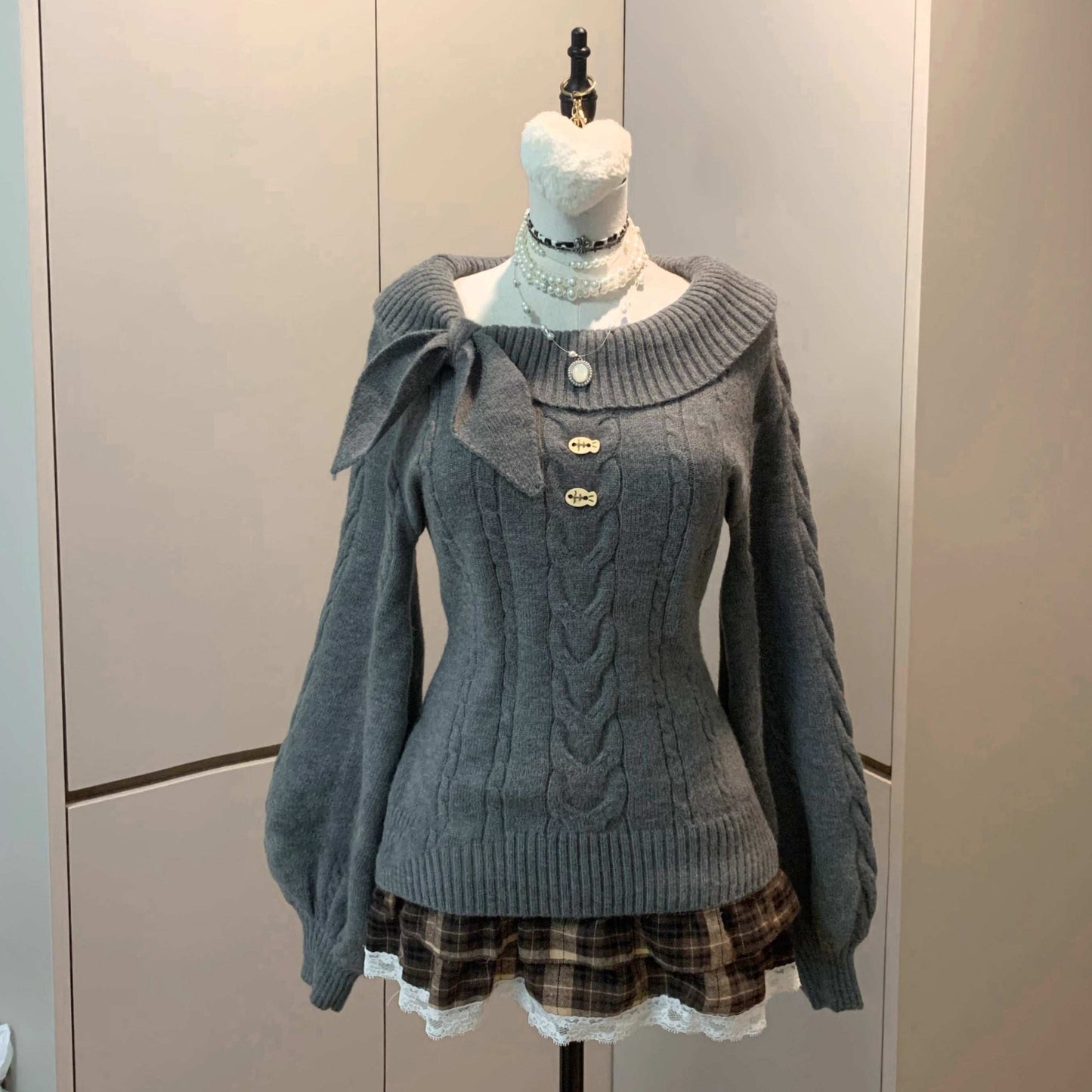 Gray sweater with a plaid skirt on a mannequin against a neutral background