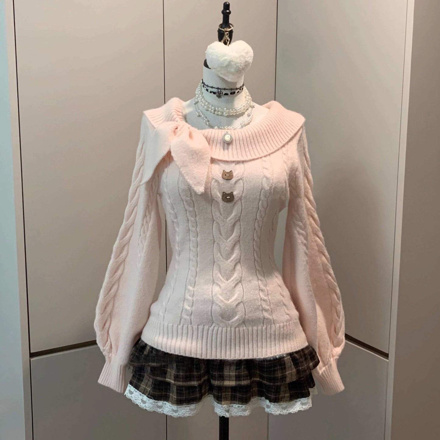 Pink cable knit sweater on a mannequin against a plain background