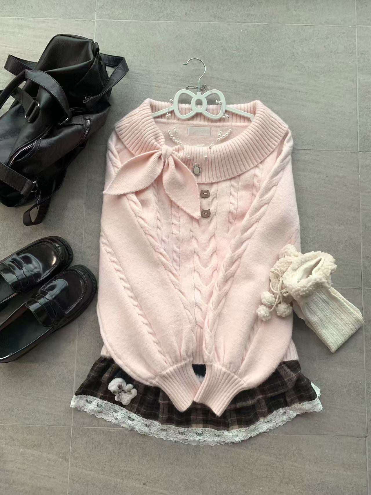 Pink sweater with a bow, black shoes, and a black bag on a gray floor.